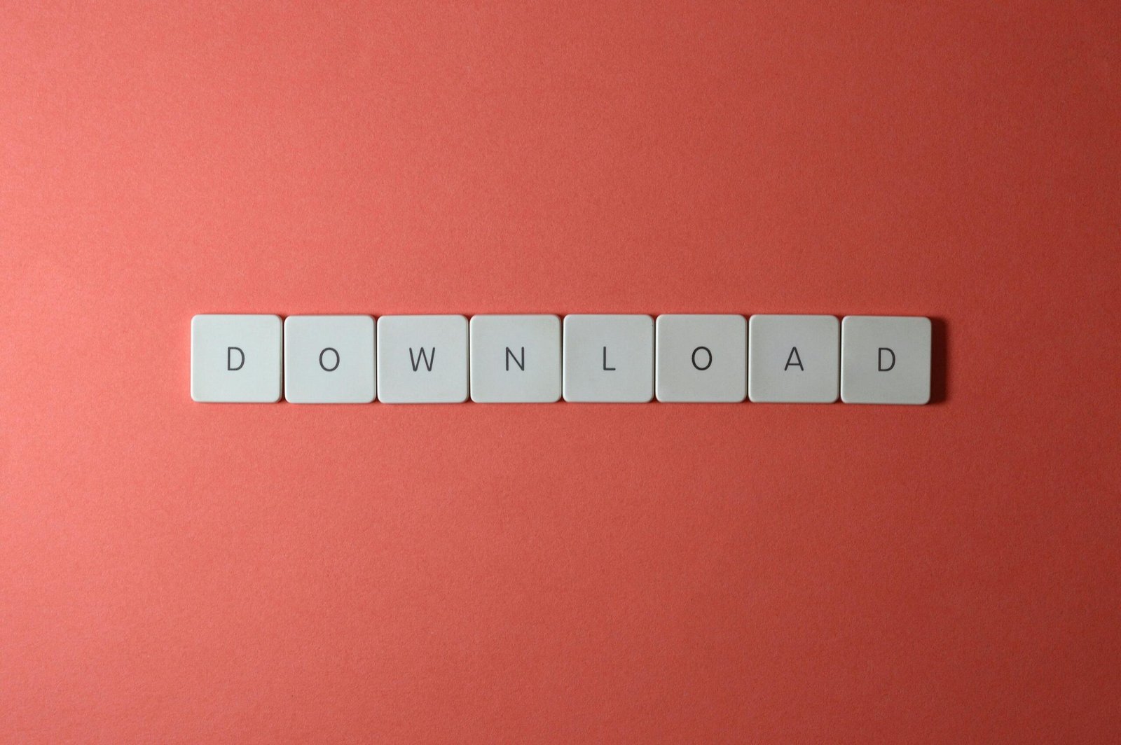 Minimalist photo of keyboard tiles spelling 'DOWNLOAD' on a red background.